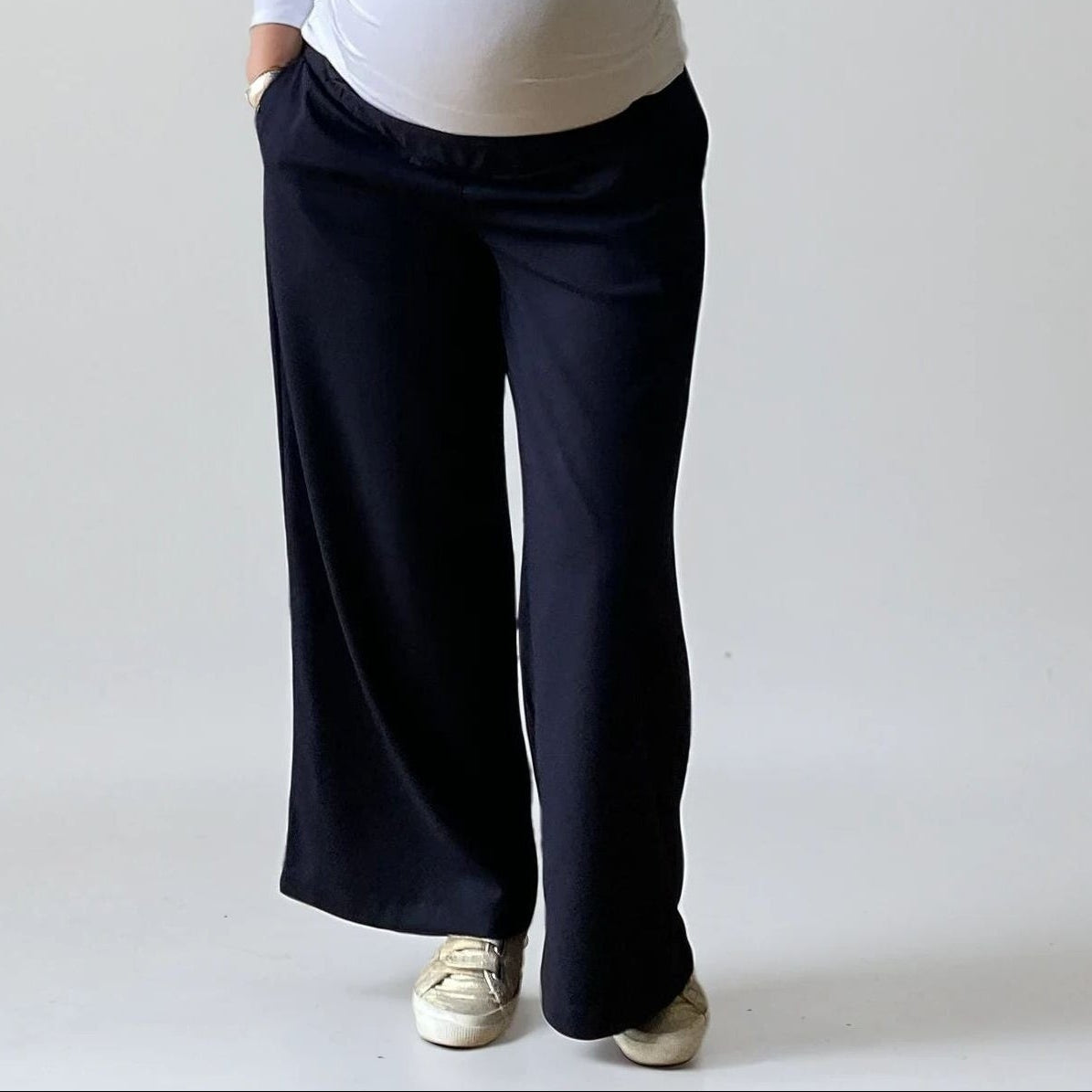 Femme enceinte portant le pantalon Eclipse bleu marine de Neuvième Ciel, coupe fluide taille basse, en studio sur fond clair. Made in France
