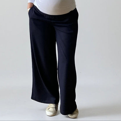 Femme enceinte portant le pantalon Eclipse bleu marine de Neuvième Ciel, coupe fluide taille basse, en studio sur fond clair. Made in France