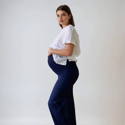 Femme enceinte portant le pantalon Cosy bleu marine, coupe droite et taille haute douce, vue de profil, sur fond studio blanc.
