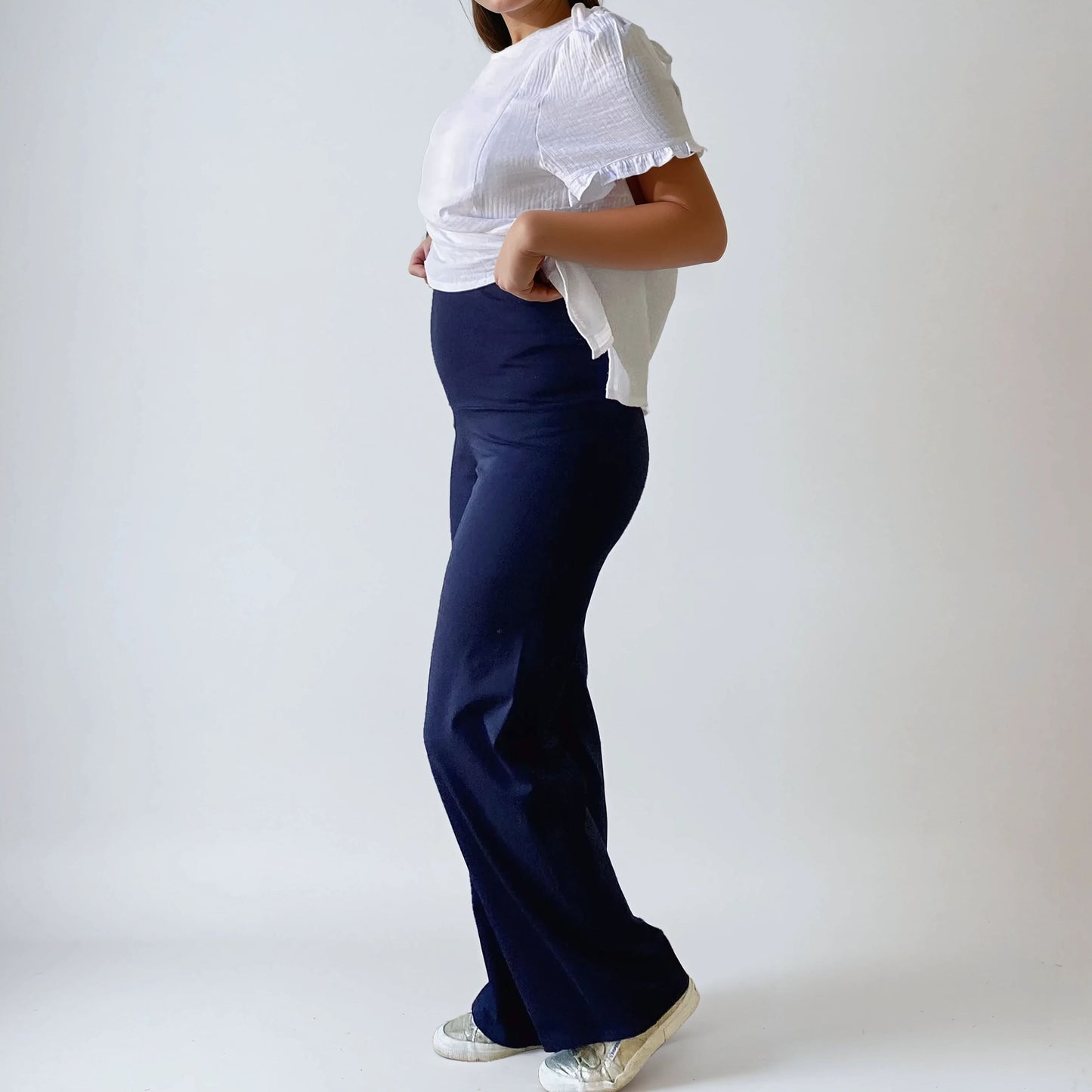 Femme enceinte portant le pantalon Cosy bleu marine, coupe droite et taille haute douce, vue de profil, sur fond studio blanc.