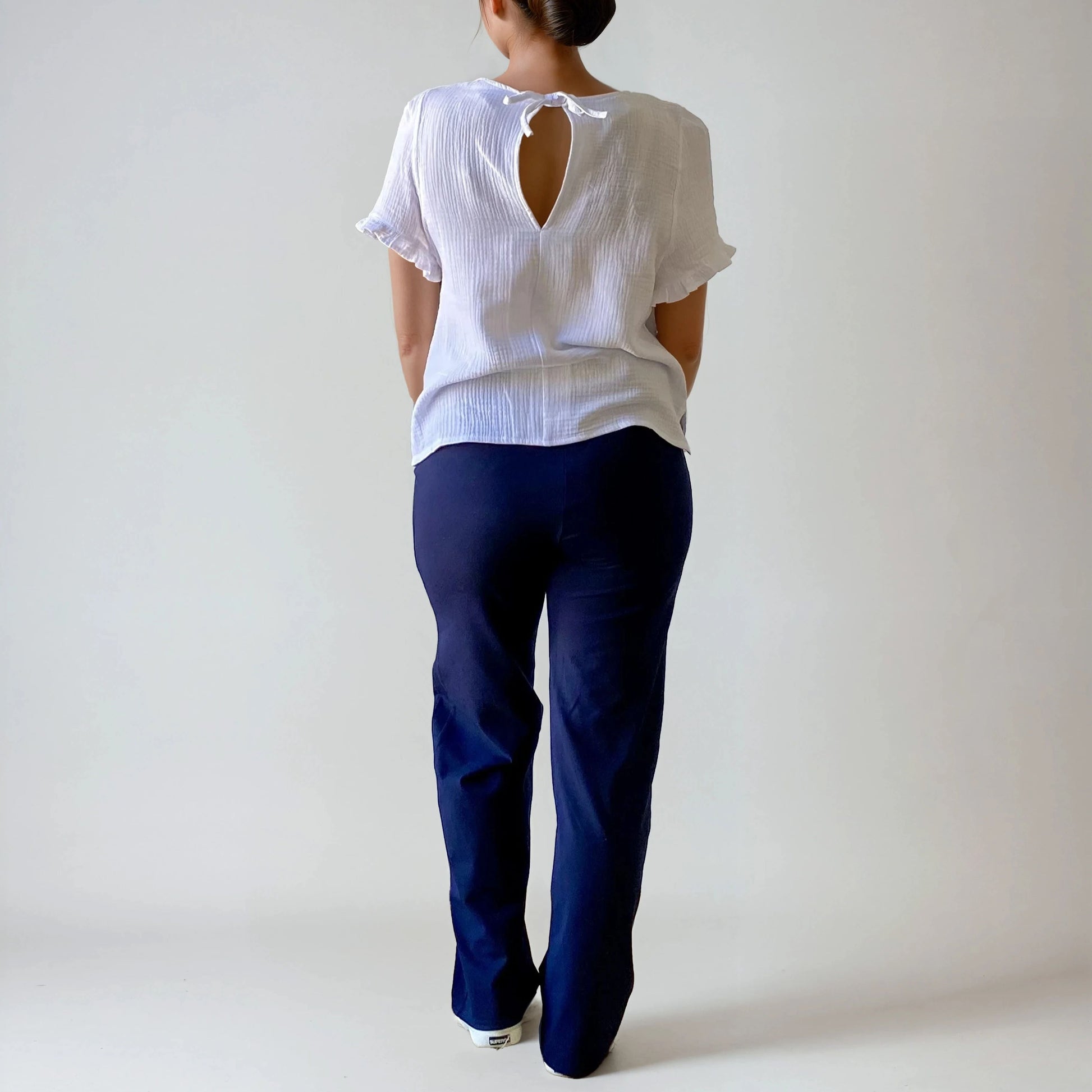 Femme enceinte de dos portant le pantalon Cosy bleu marine, coupe droite, taille haute douce et extensible, sur fond studio blanc.